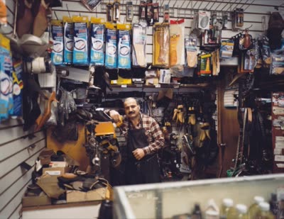 Lindsay Blatt, from Repair & Shine: shoe repairman among hanging supplies, 2008, large-format photograph.